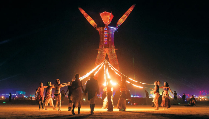 The Man illuminated at night as participants gather on the open playa