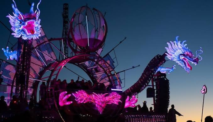 A dragon-shaped mutant vehicle lit up on the playa at night